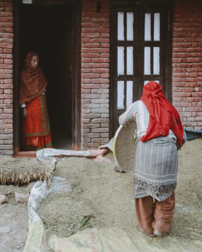 Women engaged in traditional work outside a rustic brick house in a rural village.