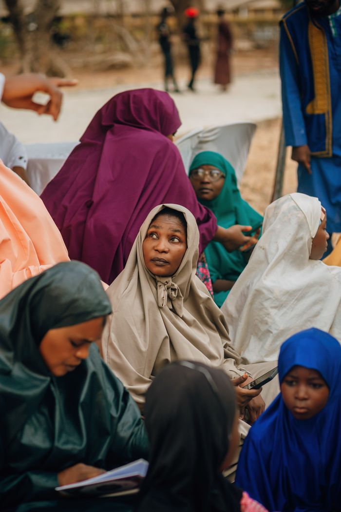 Women in colorful traditional attire participate in a community gathering outdoors.